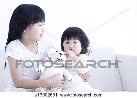 Stock Image - Girl holding her baby sister and a teddy bear. Fotosearch
