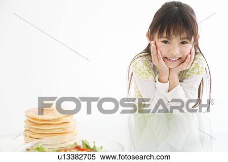 Stock Photography - Girl leaning on table next to pancake stack and salad. Fotosearch