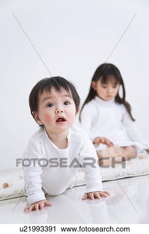 Stock Image - Girl playing with blocks on a rug next to her baby brother. Fotosearch