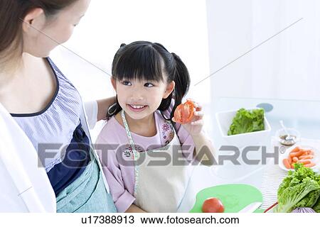 Stock Image - Girl showing mother freshly sliced tomato. Fotosearch