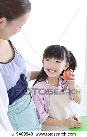 Stock Photo - Girl showing mother freshly sliced tomato. Fotosearch