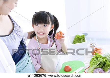 Stock Photograph - Girl showing mother freshly sliced tomato. Fotosearch