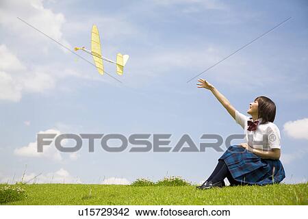 Stock Image - High school girl sitting in field throwing paper airplane. Fotosearch