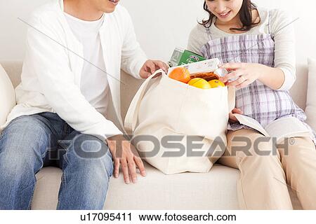 Stock Image - Husband arriving home to his pregnant wife with the groceries. Fotosearch