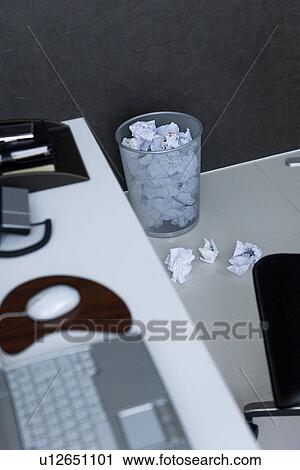 Stock Image - Laptop on desk with wastepaper basket full of crumpled paper. Fotosearch
