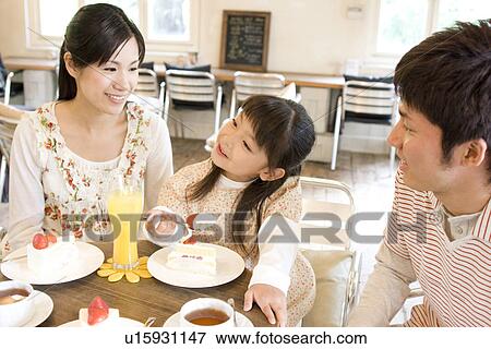 Stock Photo - Little girl eating cake at a cafe with parents. Fotosearch