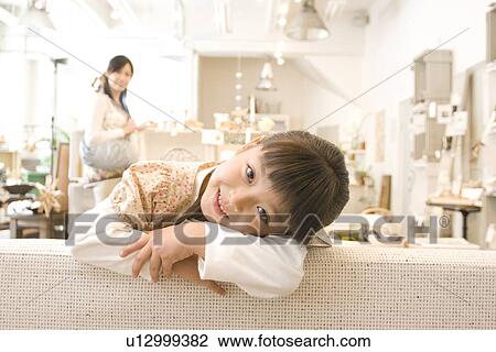 Little girl leaning over back of sofa in a furniture store with her mother shopping in the background View Large Photo Image Stock Image - Little girl leaning over back of sofa in a furniture store with her mother shopping in the background. Fotosearch