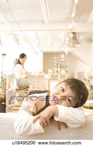 Little girl leaning over back of sofa in a furniture store with her mother shopping in the background View Large Photo Image Stock Image - Little girl leaning over back of sofa in a furniture store with her mother shopping in the background. Fotosearch