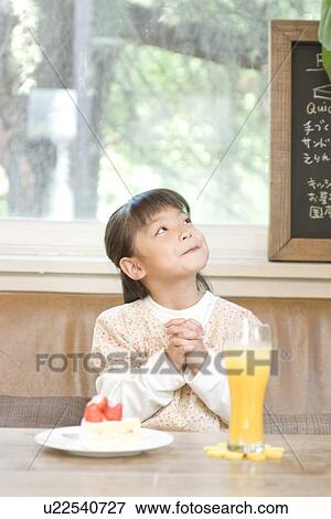 Stock Photo - Little girl sitting at cafe table with cake and juice wishing. Fotosearch