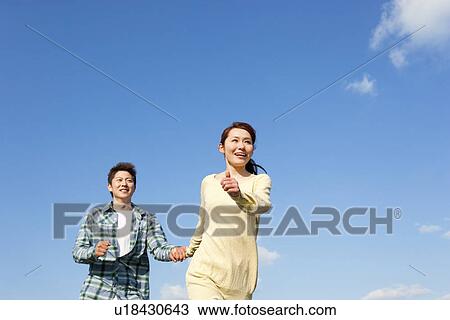Low angle view of young couple running and holding hands against a blue sky View Large Photo Image Stock Image - Low angle view of young couple running and holding hands against a blue sky. Fotosearch
