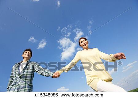 Low angle view of young couple walking and holding hands against a blue sky View Large Photo Image Stock Photograph - Low angle view of young couple walking and holding hands against a blue sky. Fotosearch