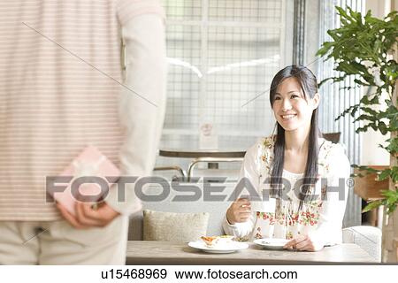 Stock Photo - Man about to give gift to his girlfriend on a date at a cafe. Fotosearch