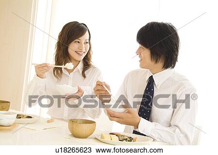 Stock Image - Man and woman eating meal at dining table. Fotosearch