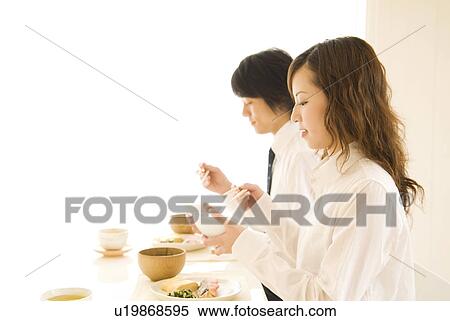 Stock Photography - Man and woman eating meal at dining table. Fotosearch