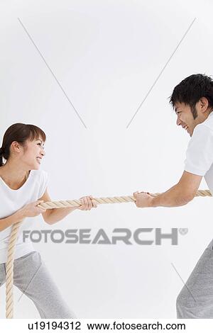 Stock Image - Man and woman playing tug-of-war. Fotosearch