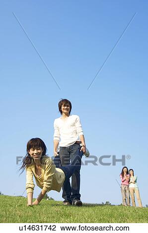 Stock Image - Man and woman playing wheelbarrow on grass. Fotosearch