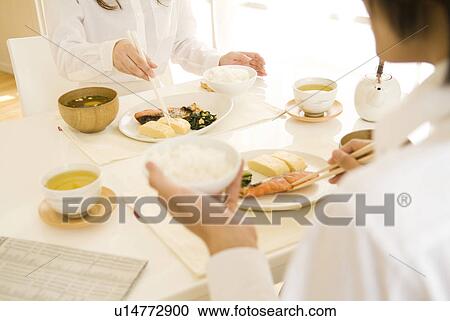 Stock Image - Man and woman sitting eating meal. Fotosearch