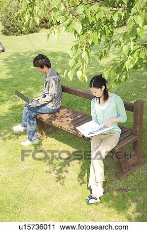 Stock Image - Man and woman sitting on bench in park. Fotosearch