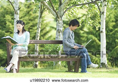 Stock Image - Man and woman sitting on bench in park. Fotosearch