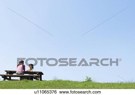 Man and woman sitting together at picnic table View Large Photo Image Stock Photograph - Man and woman sitting together at picnic table. Fotosearch