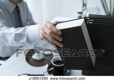 Stock Image - Man holding book in office. Fotosearch