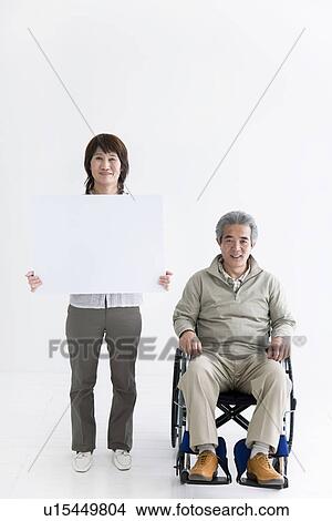 Man in a wheelchair and woman holding up blank sign View Large Photo Image Picture - Man in a wheelchair and woman holding up blank sign. Fotosearch