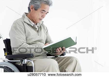 Stock Image - Man in a wheelchair reading a book. Fotosearch