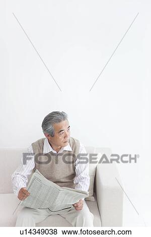 Stock Photo - Man reading newspaper on sofa. Fotosearch