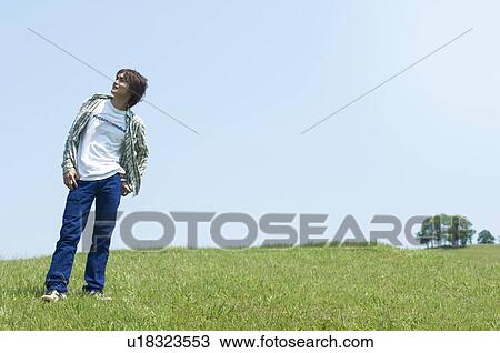 Stock Image - Man standing on grass looking into distance. Fotosearch