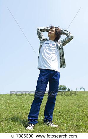 Stock Image - Man standing on grass with hands behind head. Fotosearch
