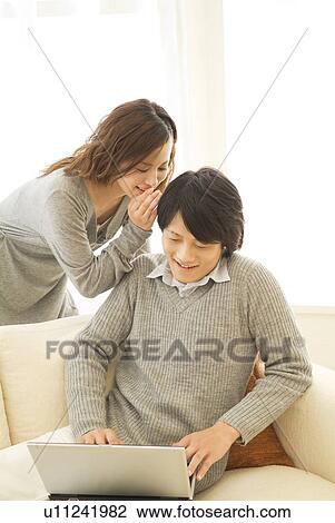 Man using a laptop while woman whispers in his ear View Large Photo Image Stock Image - Man using a laptop while woman whispers in his ear. Fotosearch
