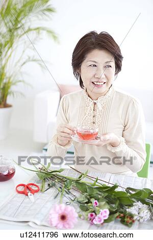 Stock Photograph - Mature woman drinking tea and arranging flowers. Fotosearch
