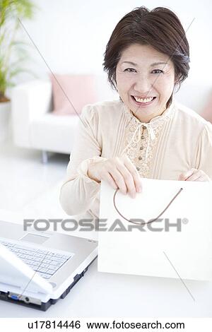 Stock Photograph - Mature woman smiling with a gift bag. Fotosearch
