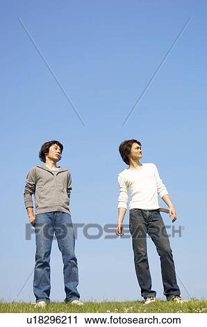 Stock Image - Men standing on grass gazing into distance. Fotosearch