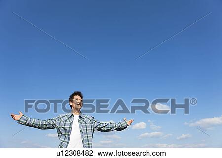 Stock Image - Mid adult man spreading his arms under a blue sky. Fotosearch