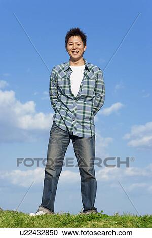 Stock Image - Mid adult man with his hands behind his back under a blue sky. Fotosearch