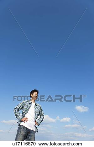 Stock Image - Mid adult man with his hands on his hips under a blue sky. Fotosearch