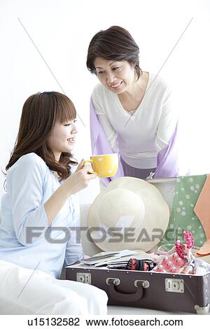 Stock Image - Mother and daughter drinking coffee on a sofa. Fotosearch