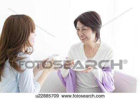 Mother and daughter sitting on sofa and drinking coffee View Large Photo Image Stock Photo - Mother and daughter sitting on sofa and drinking coffee. Fotosearch