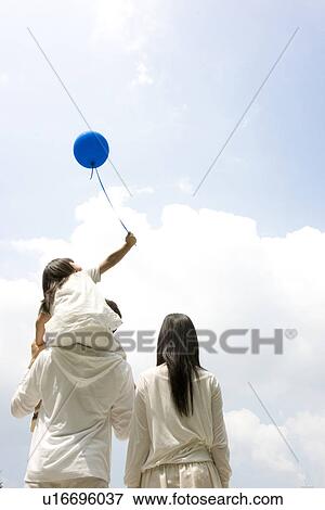 Mother and father carrying daughter on his shoulders holding a balloon View Large Photo Image Stock Photo - Mother and father carrying daughter on his shoulders holding a balloon. Fotosearch