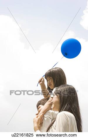 Stock Photography - Mother and father carrying daughter on his shoulders holding a balloon. Fotosearch
