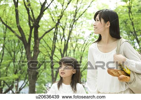 Stock Photo - Mother carrying grocery bag and daughter walking through park. Fotosearch