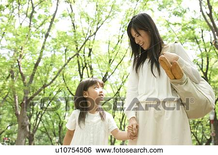 Stock Photograph - Mother carrying grocery bag and daughter walking through park. Fotosearch