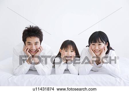 Picture - Mother, father and daughter lying on bed. Fotosearch