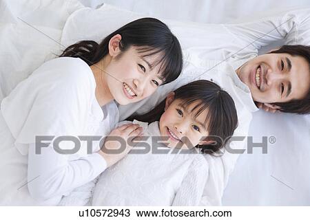 Mother, father and daughter lying on bed View Large Photo Image Stock Image - Mother, father and daughter lying on bed. Fotosearch