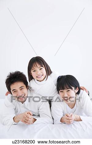 Stock Image - Mother, father and daughter lying on bed. Fotosearch