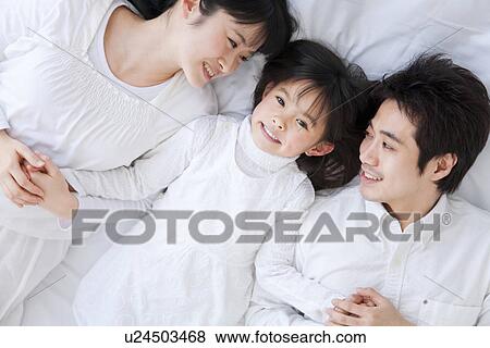 Stock Photo - Mother, father and daughter lying on bed. Fotosearch