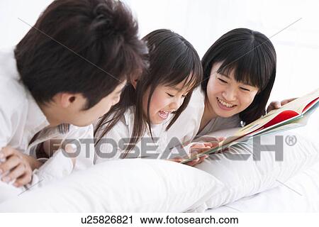 Mother, father and daughter lying on bed reading picture book View Large Photo Image Stock Image - Mother, father and daughter lying on bed reading picture book. Fotosearch