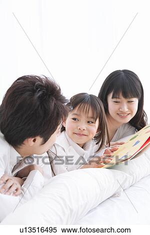 Mother, father and daughter lying on bed reading picture book View Large Photo Image Stock Photography - Mother, father and daughter lying on bed reading picture book. Fotosearch