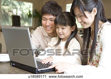 Stock Image - Mother, father and daughter using laptop at a cafe. Fotosearch